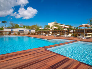 Outdoor swimming pool with wooden deck, sun loungers, and umbrellas at Milano Marittima Boutique Resort under blue sky