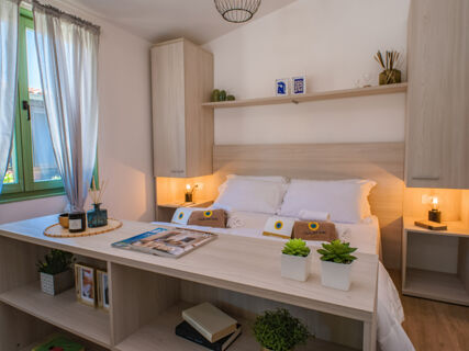 Bedroom area with white bed linens, wooden shelves, potted plants, decorative items, and a green window at Milano Marittima Boutique Resort