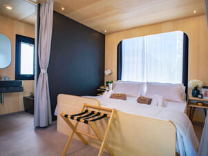 Modern hotel room at Milano Marittima Boutique Resort with wooden bed frame, white linens, luggage rack, and large window with curtains