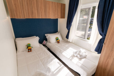 Two single beds with white bedding and stuffed frogs are side by side under wooden cabinets next to a window at Rivaverde Easy Camping Village