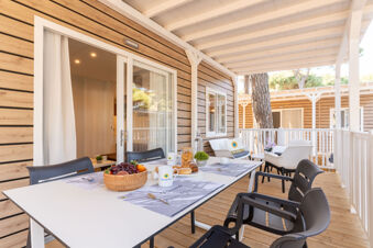 Outdoor seating area with a white table, black chairs, breakfast items, and wooden exterior walls at Rivaverde Easy Camping Village