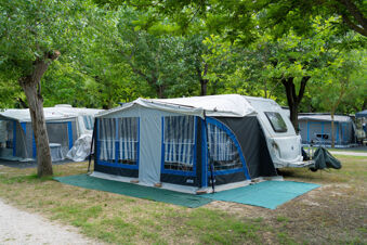 Caravan with a large blue and gray attached awning among green trees at Adriatico Cervia Easy Camping Village campsite