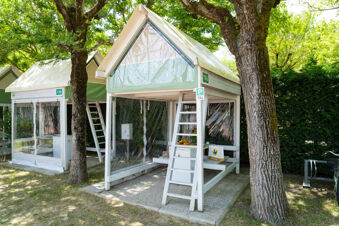 Two small green and white triangular roofed tents with transparent plastic walls under trees at Adriatico Cervia Easy Camping Village