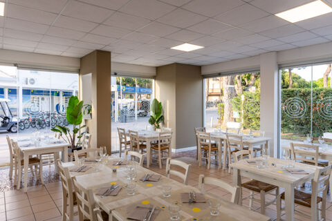 Dining area with wooden tables and chairs set with glasses and cutlery inside Adriatico Cervia Easy Camping Village restaurant
