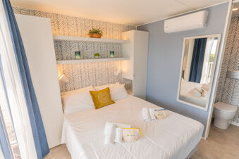 Double bed with white linens and a yellow pillow in a room with patterned wallpaper shelves and a wall mirror at Vigna sul Mar Family Collection