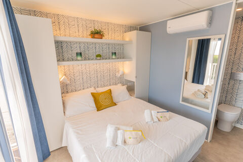 Double bed with white linens and a yellow pillow in a room with patterned wallpaper shelves and a wall mirror at Vigna sul Mar Family Collection
