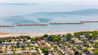 Aerial view of a beach with umbrellas, people swimming, stone breakwaters, and holiday homes near Vigna sul Mar Family Collection
