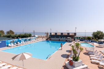 Bright swimming pool area with sun loungers, umbrellas, and a woman walking at Roseto degli Abruzzi Easy Camping Village