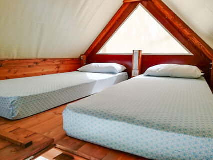 Two single beds with white pillows and patterned sheets inside a wooden A-frame tent at Roseto degli Abruzzi Easy Camping Village