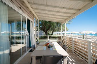 Outdoor covered balcony with a dining table set for breakfast overlooking beach umbrellas and the sea at La Risacca Family Collection