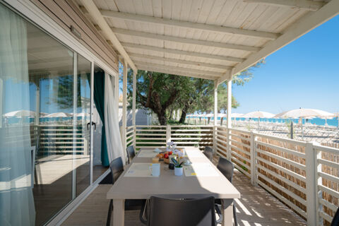 Outdoor covered balcony with a dining table set for breakfast overlooking beach umbrellas and the sea at La Risacca Family Collection