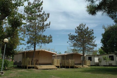 Two beige canvas tents with wooden decks and chairs surrounded by trees and grass at La Risacca Family Collection