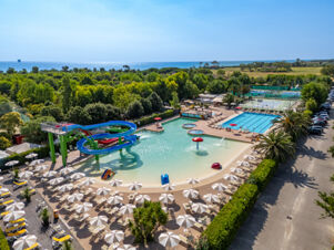 Outdoor water park with a large pool, water slides, sun umbrellas, tennis courts, and greenery near the sea at La Risacca Family Collection