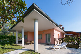 Outdoor patio area with white columns, a wooden picnic table, and a white lounge chair at Le Palme Lazise Family Collectio