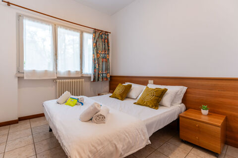 Double bed with white linens and green pillows next to a window with floral curtains at Le Palme Lazise Family Collectio