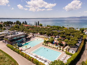 Aerial view of two swimming pools, water slides, lounge chairs, umbrellas, playground, and lake shore at Le Palme Lazise Family Collectio