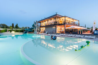 Outdoor pool area with water slide, children's pool, sun loungers, and illuminated building at Le Palme Lazise Family Collectio