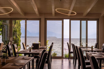 Dining area with dark chairs, wooden tables with flowers, large windows overlooking a lake and mountains at Desenzano Boutique Resor