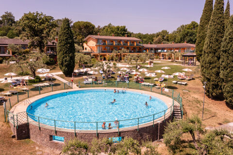 Round outdoor pool with people swimming and sunbathing near a multi-story building surrounded by trees at Desenzano Boutique Resor