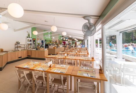 Dining area with wooden tables and chairs, pendant lights, ceiling fans, and a food counter at Jesolo Family Resort