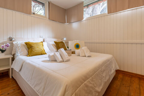 White bed with mustard yellow pillows, rolled towels, bedside tables, two windows with brown curtains in Jesolo Family Resort room