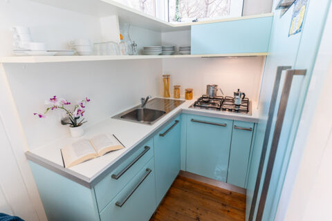 Small kitchen with light blue cabinets, open shelves with cups and plates, sink, stove, and glass jars at Jesolo Family Resort