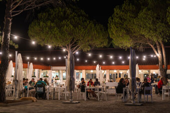People dining outside at night under string lights and pine trees at Marina Julia Family Collection restaurant area