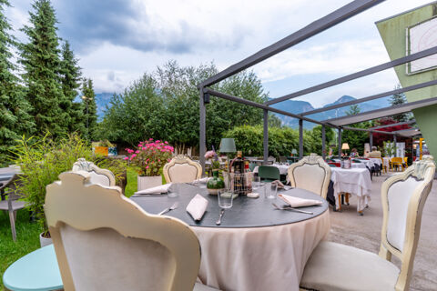 Outdoor dining area with tables, chairs, plants, and mountains in the background at Due Laghi Levico Family Collection