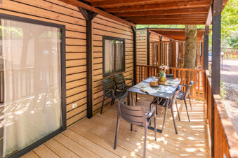 Outdoor wooden patio with black chairs and a table set with cups, fruit, and an open book at Due Laghi Levico Family Collection