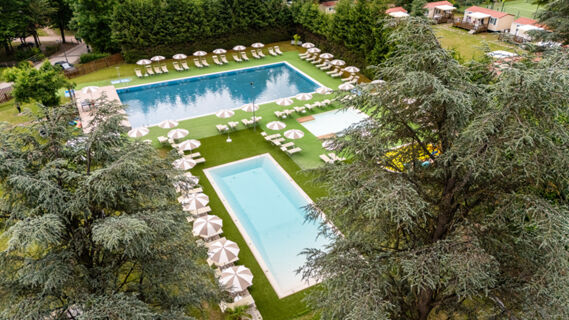 Outdoor view of three swimming pools surrounded by empty lounge chairs and beige umbrellas at Due Laghi Levico Family Collection