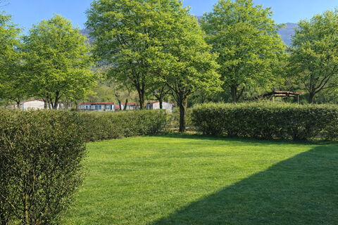 Green grass lawn with neatly trimmed bushes and several leafy trees near mobile homes at Due Laghi Levico Family Collection