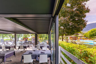Outdoor dining area with tables and chairs under a covered patio next to swimming pool and playground at Caldonazzo Family Collection