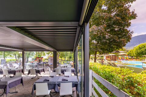 Outdoor dining area with tables and chairs under a covered patio next to swimming pool and playground at Caldonazzo Family Collection