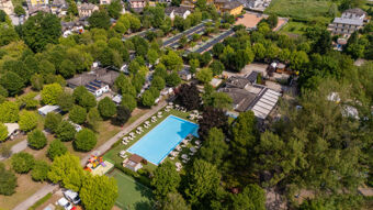 Aerial view of Caldonazzo Family Collection featuring a large outdoor pool with umbrellas, green trees, playground, and surrounding buildings