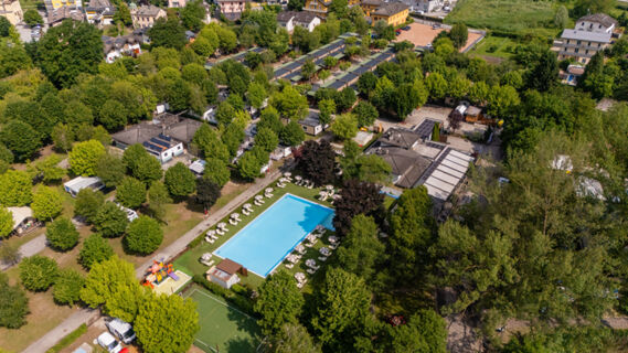 Aerial view of Caldonazzo Family Collection featuring a large outdoor pool with umbrellas, green trees, playground, and surrounding buildings
