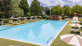 Outdoor swimming pool with beige lounge chairs and umbrellas surrounded by green trees at Caldonazzo Family Collection