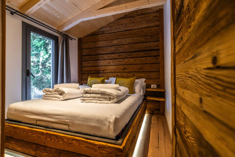 Bedroom at Val di Fiemme Easy Camping Village featuring a wooden bed frame with white bedding and green pillows next to a window
