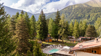An outdoor pool with sun loungers and umbrellas surrounded by trees and wooden cabins at Val di Fiemme Easy Camping Village