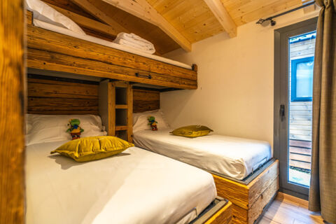 Two single beds with white linens, yellow pillows, wooden bunk bed frames, and a glass door at Val di Fiemme Easy Camping Village