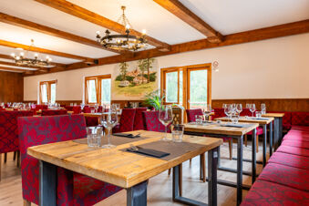 Dining area with wooden tables, red patterned chairs, chandeliers, and a mural on the wall at Val di Fiemme Easy Camping Village