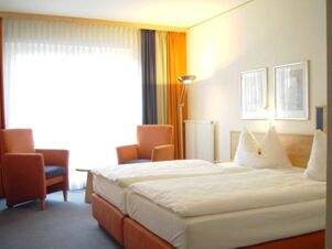 Bright hotel room at Akzent Hotel Stadt Schl&uuml;chtern with two single beds, two orange armchairs, and large window with curtains