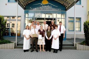 Групповая фотография сотрудников и руководства отеля перед входом в Akzent Hotel Stadt Schl&uuml;chtern с наградами в руках.
