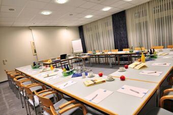 Meeting room with white tables arranged in a U-shape, wooden chairs, notebooks, apples, and bottles at Akzent Hotel Stadt Schl&uuml;chtern