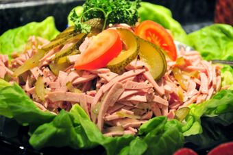 Sliced meat salad garnished with pickle slices, tomato wedges, and parsley on a bed of lettuce leaves at Akzent Hotel Stadt Schl&uuml;chtern
