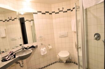 Bathroom at Akzent Hotel Stadt Schl&uuml;chtern with white tiled walls, a toilet, sink with mirror, and a glass shower door