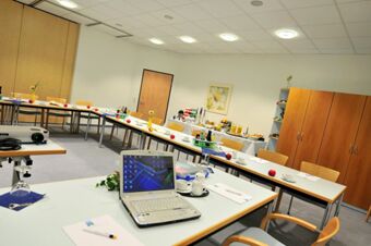 Конференц-зал с ноутбуком, чашками и закусками, оборудованный для проведения совещаний в отеле Akzent Hotel Stadt Schl&uuml;chtern и обставленный мебелью в светлых тонах.