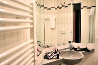 Black high-heeled sandals and a perfume bottle placed on the sink countertop inside a tiled bathroom at Akzent Hotel Stadt Schl&uuml;chtern