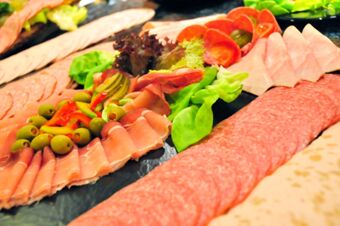 Assorted sliced deli meats with green olives, pickles, and leafy greens served on a platter at Akzent Hotel Stadt Schl&uuml;chtern