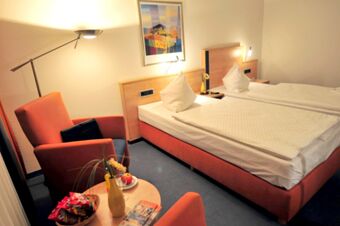 Hotel room at Akzent Hotel Stadt Schl&uuml;chtern with twin beds, orange armchairs, a round table, and a standing lamp