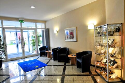 Lobby area of Akzent Hotel Stadt Schl&uuml;chtern with black chairs, wooden tables, a glass display case, and a large glass entrance door